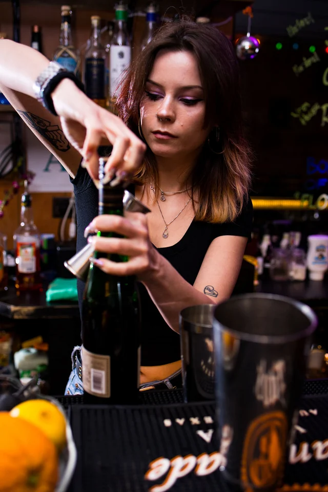 A bartender measures a bottle pour over a metal shaker.