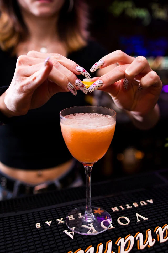 A bartender twists a citrus peel over an orange cocktail.