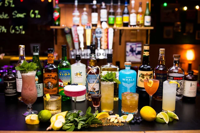 A full bar-top lineup of colorful cocktails, fruit and spirits.