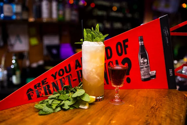 A mint-topped highball and a small coupe in front of a red Fernet-Branca pennant.