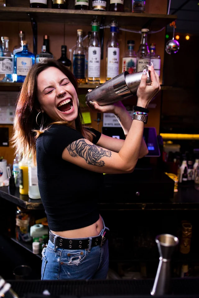 A laughing bartender shakes a cocktail behind the Easy Tiger bar.