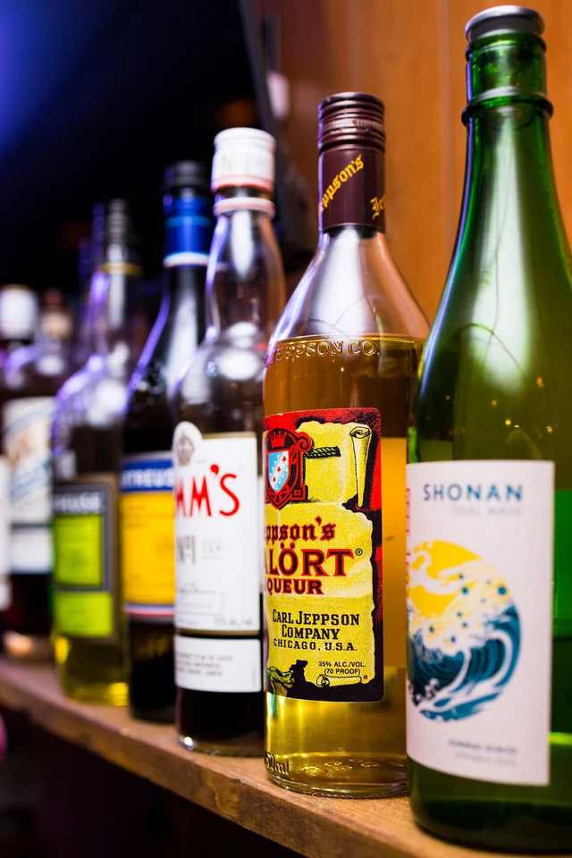 A row of liqueur and spirit bottles on a wooden bar shelf.