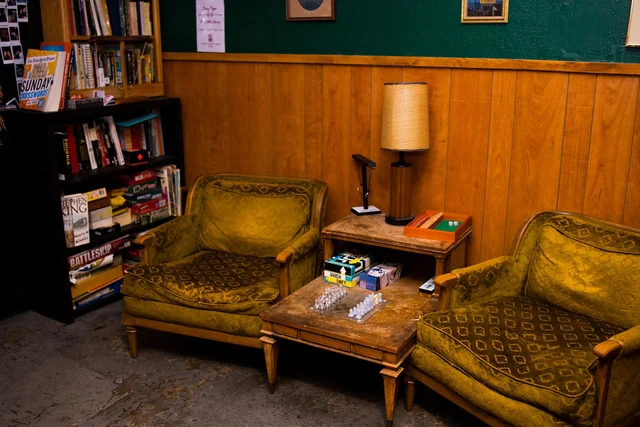 Green lounge chairs, books, games and a lamp around a low wooden table.