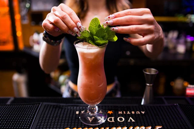 Hands arrange fresh mint on a curved cocktail glass.