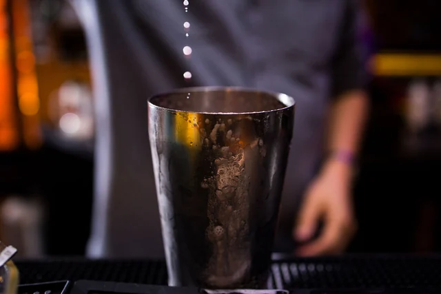 Drops fall from a bar spoon into a metal shaker.