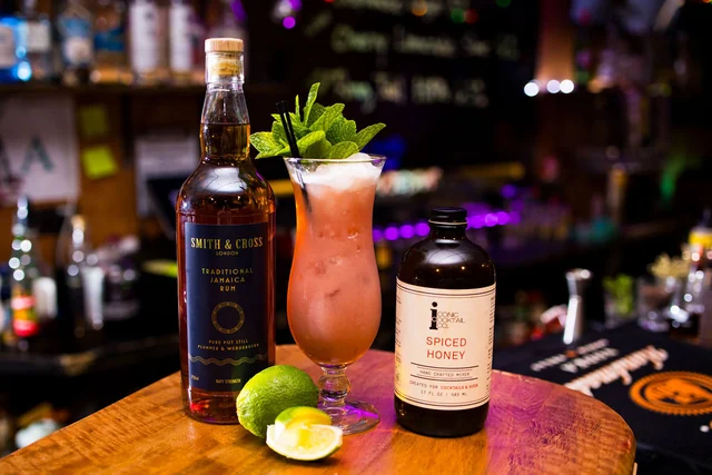 A mint-topped cocktail beside Smith & Cross rum and Spiced Honey.