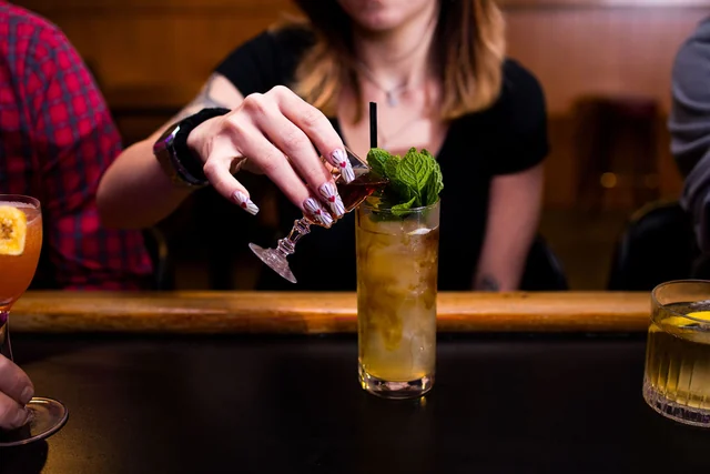 A guest tips a small cordial glass into a mint-topped highball.