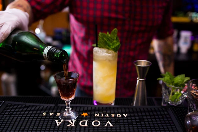 Sparkling wine pours from a green bottle beside two cocktails.