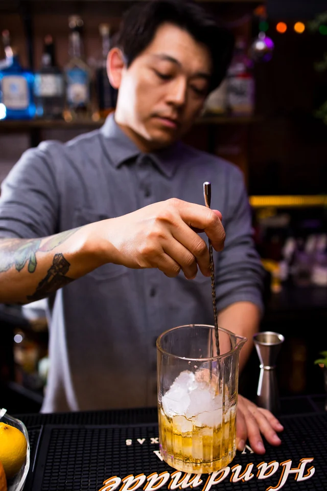 A bartender stirs a mixing glass filled with ice.