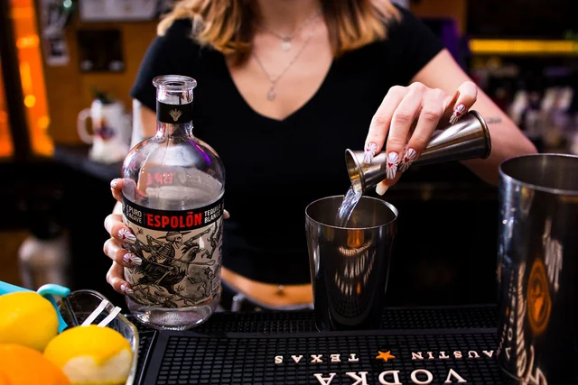 A bartender measures Espolòn tequila into a metal shaker.