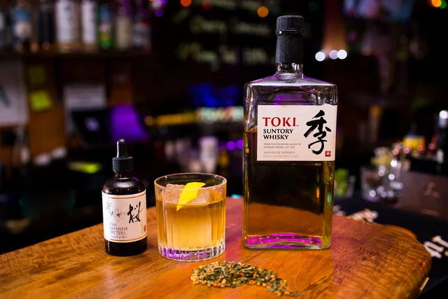 Toki whisky beside a short golden cocktail, lemon and herbs.