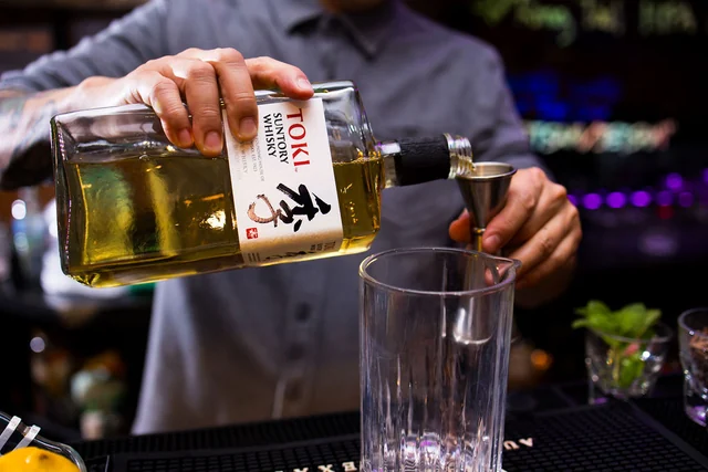A bartender pours Toki whisky into a jigger over a mixing glass.