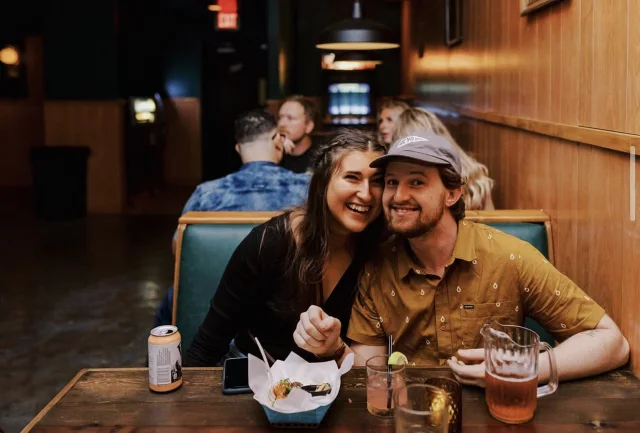 Two guests smiling in a booth with food and drinks.